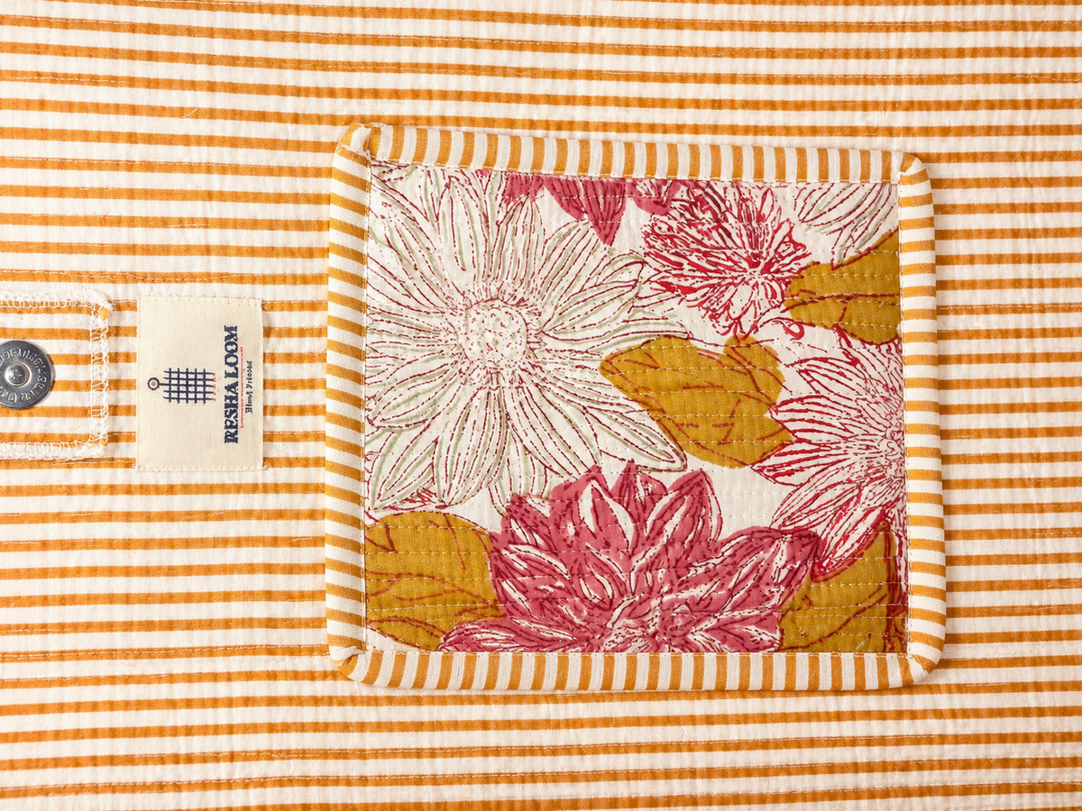 A close-up of a quilted fabric bag, featuring a central floral compartment design with pink and mustard yellow flowers on a white background, surrounded by a striped border.
