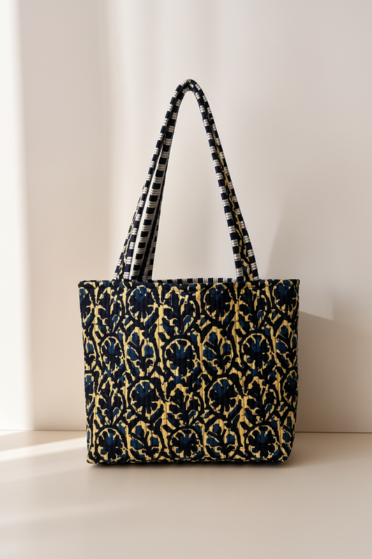 A structured tote bag with a navy blue and gold floral damask pattern, featuring thick woven shoulder straps with black and white stripes.