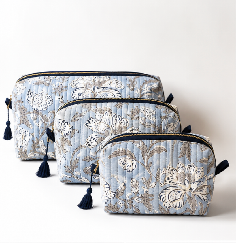 Three quilted cosmetic pouches in a nested set, featuring a light blue background with a beige and white floral pattern and navy blue tassels on the zipper pulls, set against a plain light background.