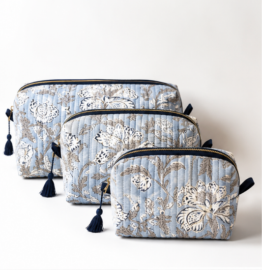 Three quilted cosmetic pouches in a nested set, featuring a light blue background with a beige and white floral pattern and navy blue tassels on the zipper pulls, set against a plain light background.