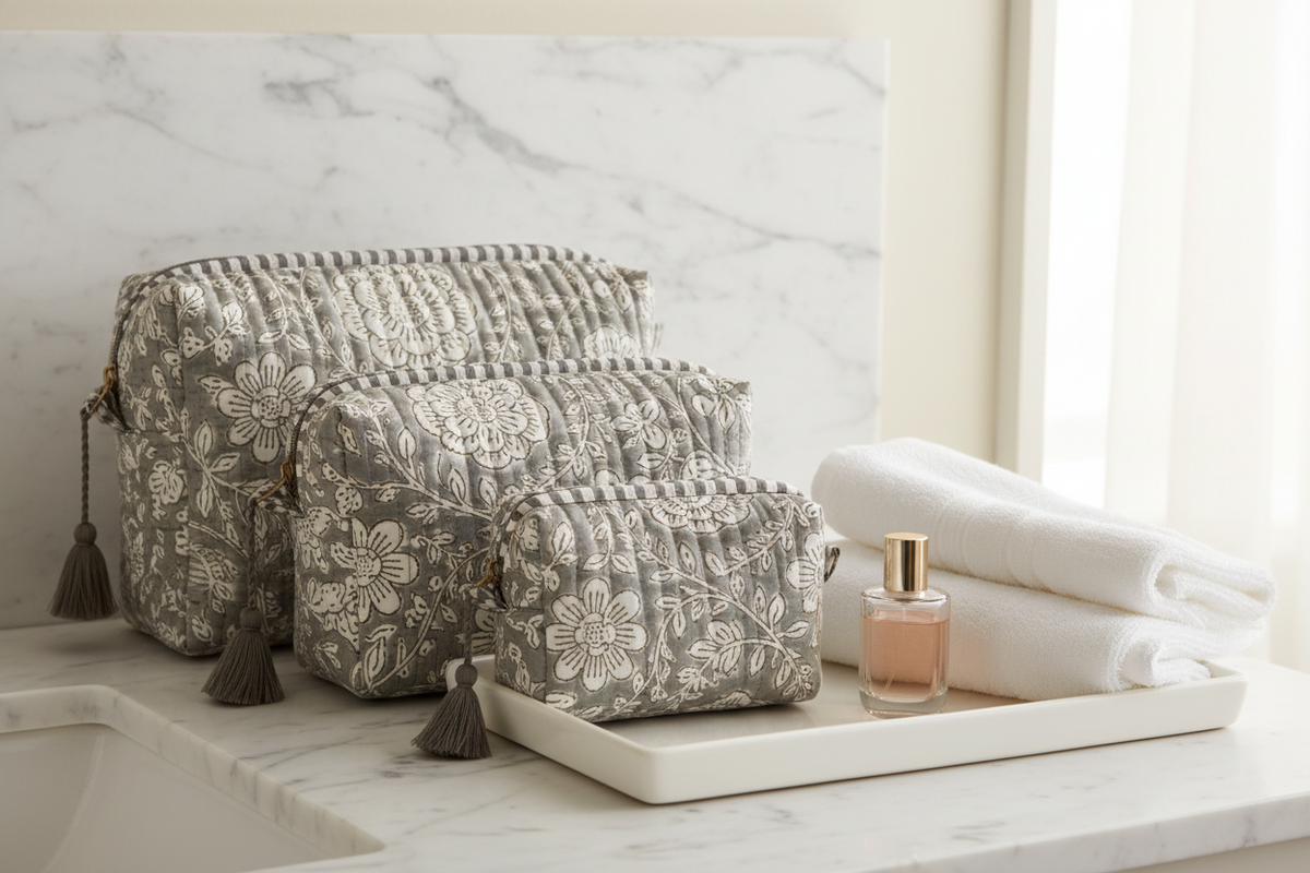 Three quilted cosmetic pouches in a nested set, featuring a gray and white floral pattern, striped top borders, and dark gray tassels on the side.
