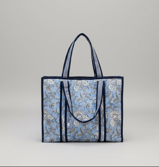 Floral patterned tote bag with blue straps on a light blue background 