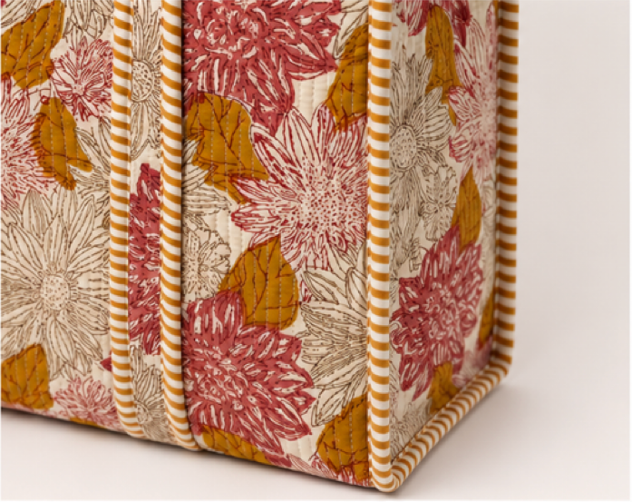 Close-up of a fabric-covered box or organizer with a floral print in dusty pink, mustard yellow, and beige, finished with striped trim.