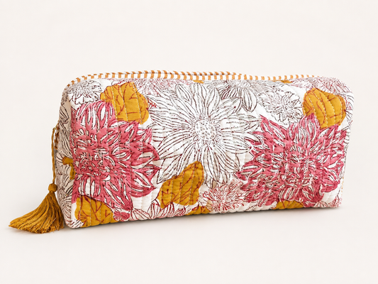 A quilted cosmetic pouch with a floral print in pink, mustard yellow, and white, featuring a tassel zipper pull on a light beige background.