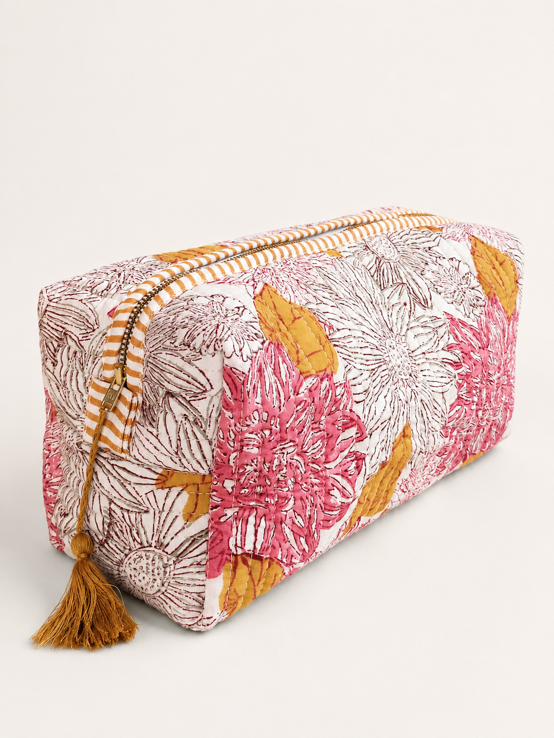 A rectangular zippered cosmetic pouch with a colorful floral print in pink, mustard yellow, and brown on a white background, featuring a striped zipper and a tassel.