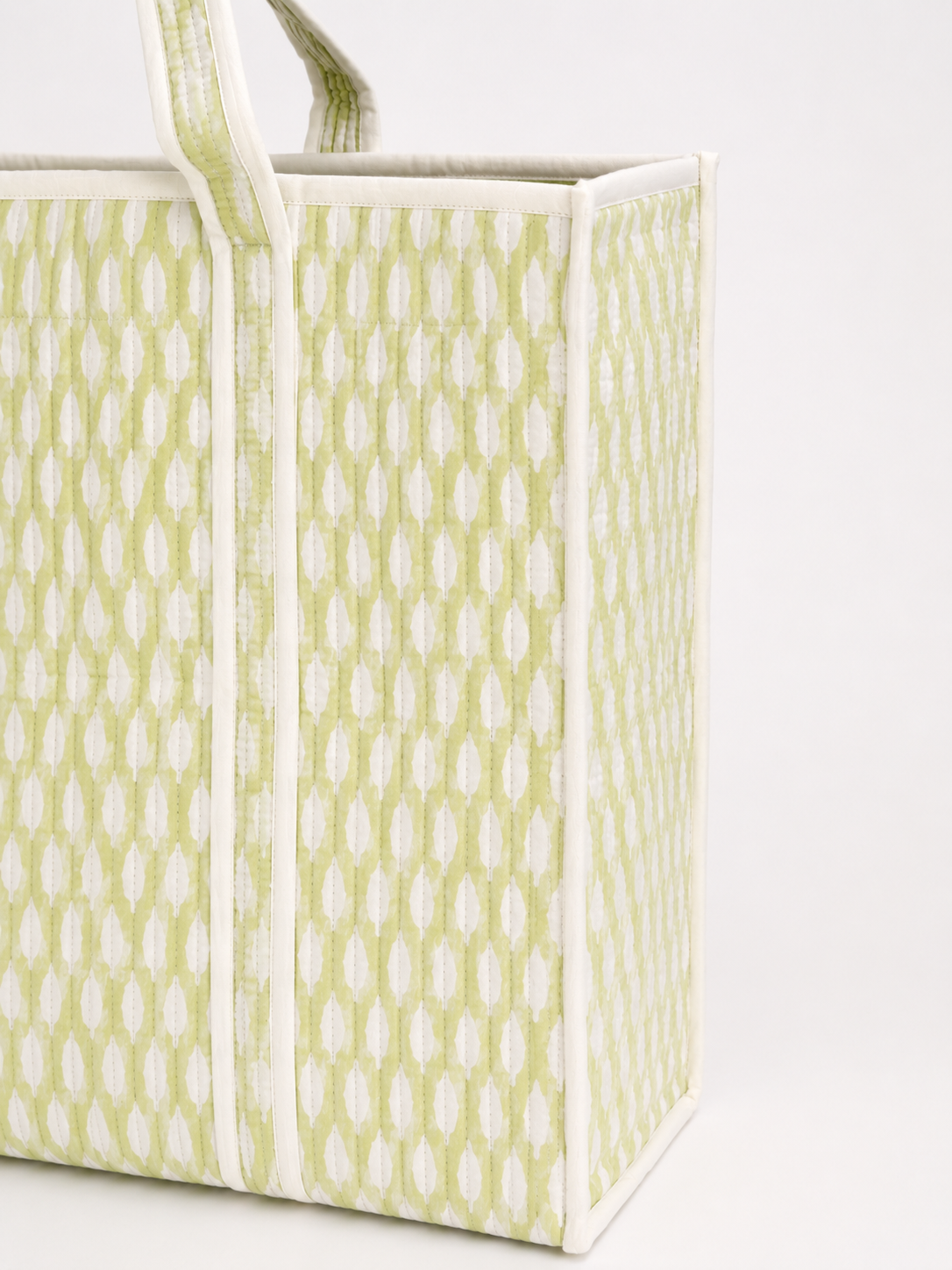A close-up of a fabric tote bag with a light green and white repeating buti pattern and white trim.