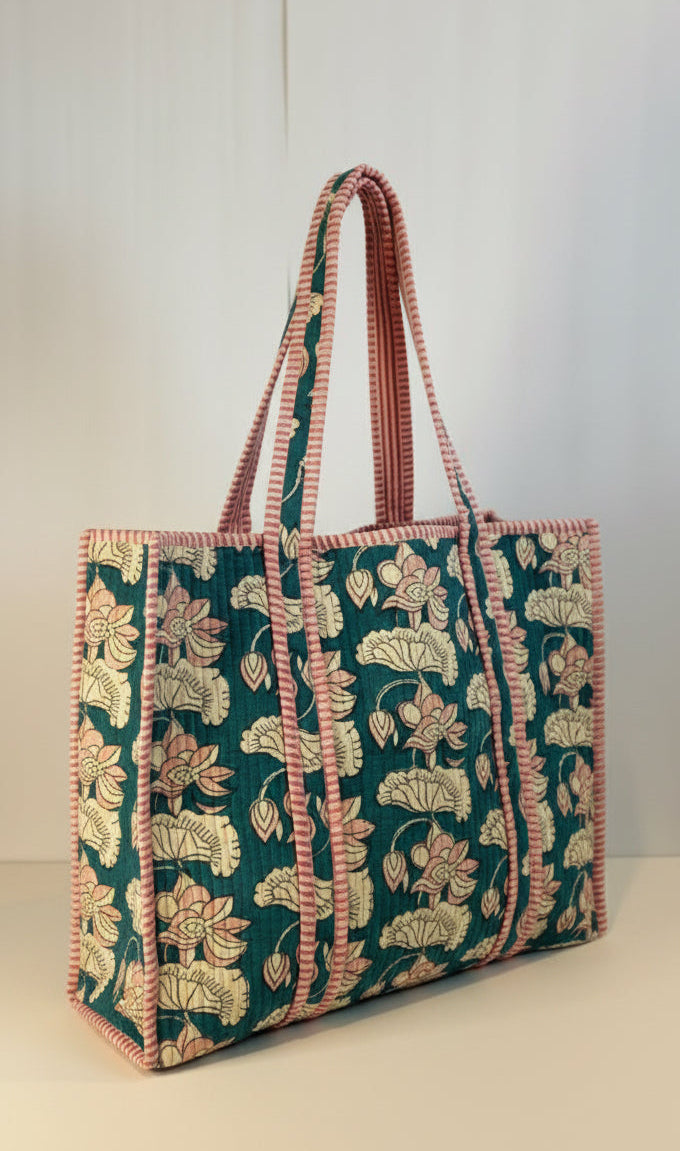 A fabric tote bag with a dark teal green background, decorated with a cream and pink floral pattern, and featuring pink and cream striped handles.