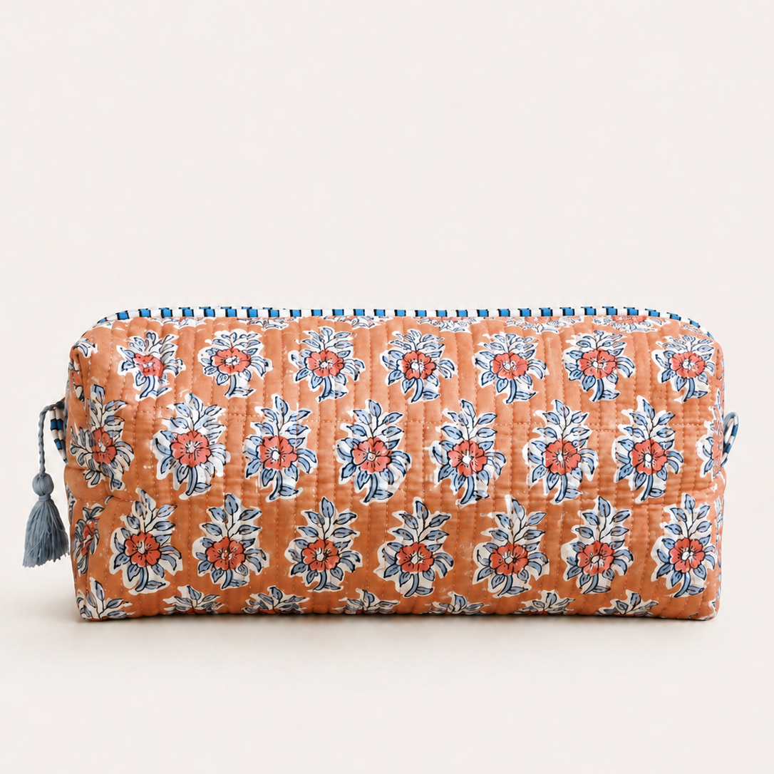 A quilted cosmetic pouch with an orange base, featuring a repeating blue and red floral block print pattern, zipper, and a blue tassel on the side