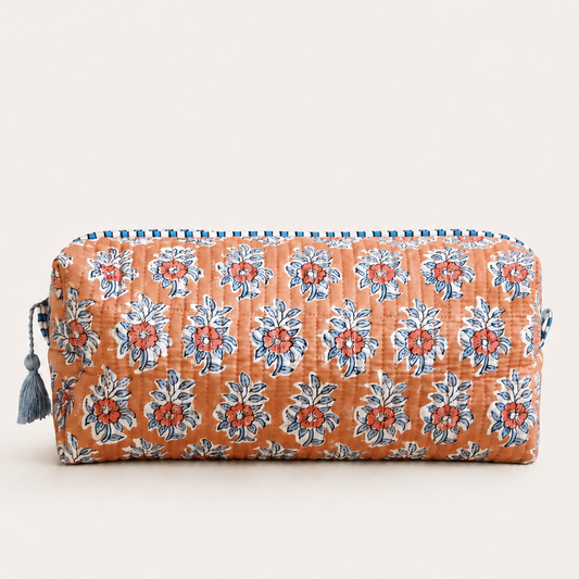 A quilted cosmetic pouch with an orange base, featuring a repeating blue and red floral block print pattern, zipper, and a blue tassel on the side