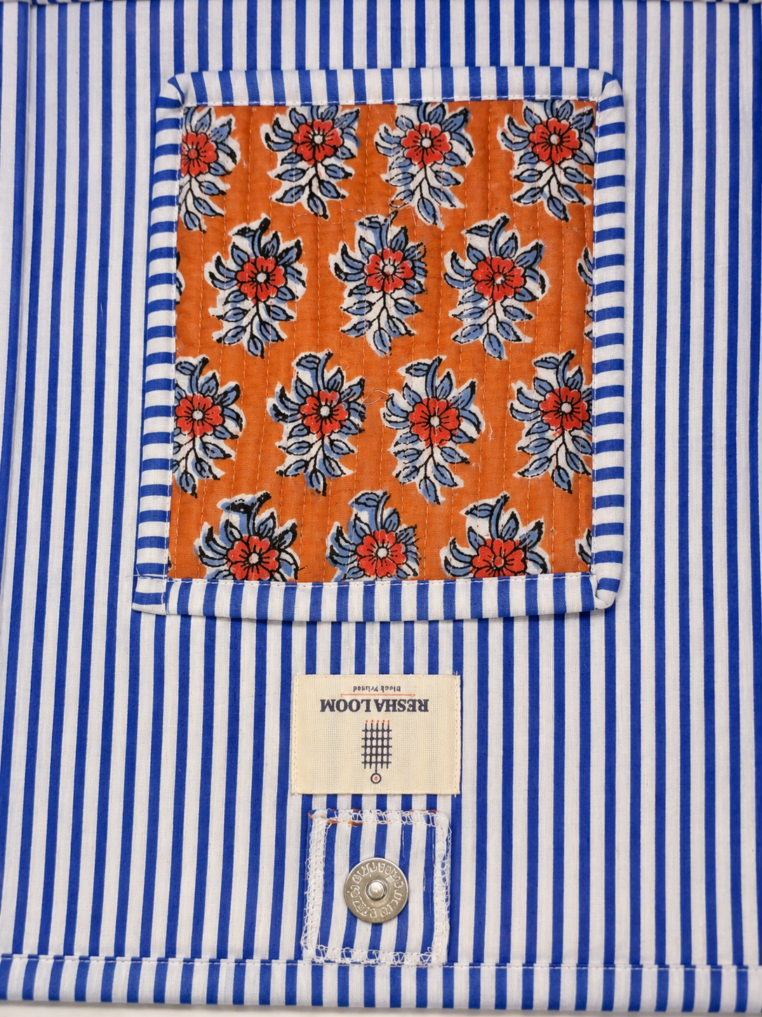 A hand block printed tote bag , featuring a inside of the bag, blue and white vertical stripe pattern with a square orange pocket printed with red and blue floral print